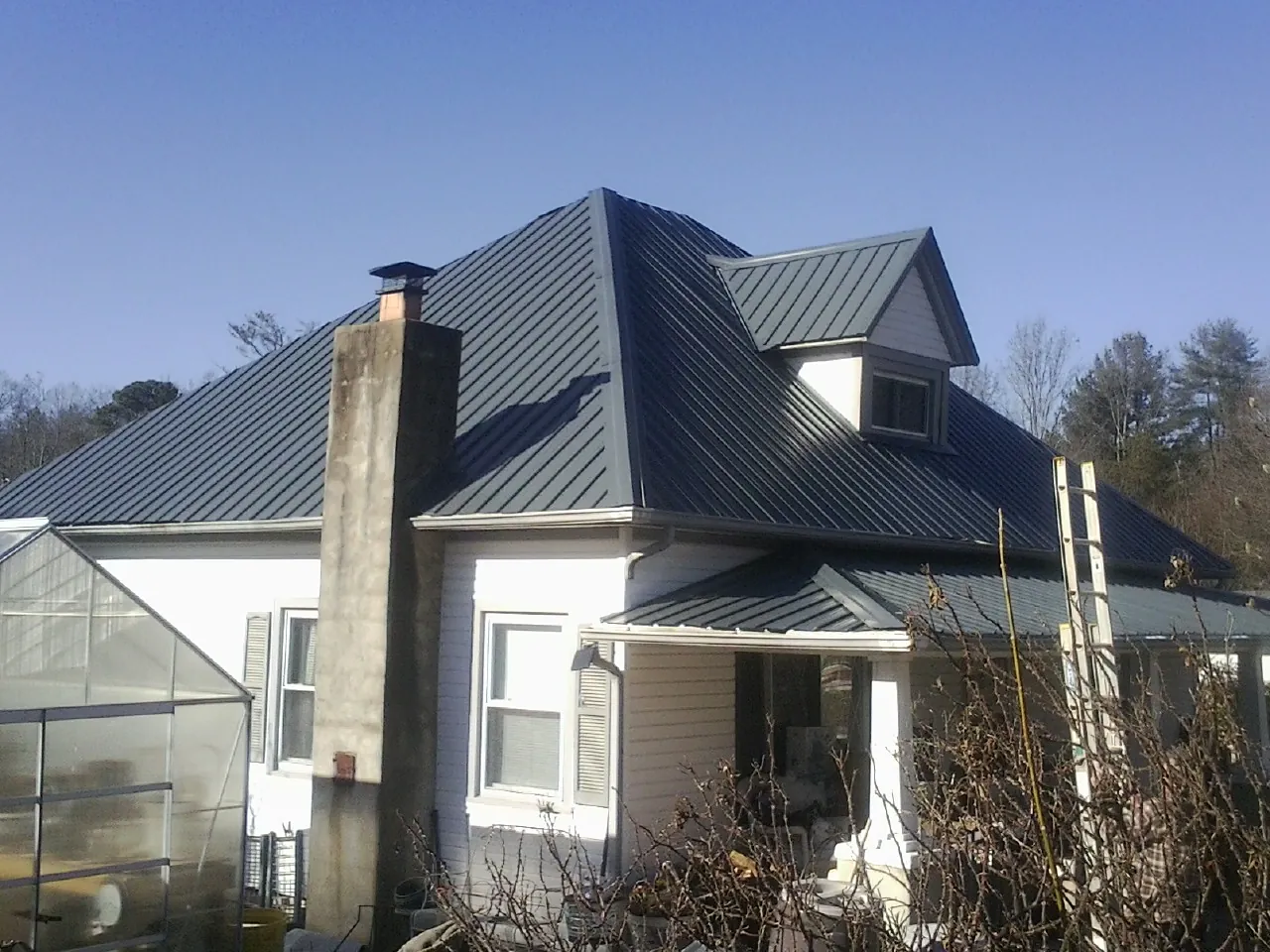 Dark blue standing seam metal roof on a white farmhouse with dormer — Slate & Tile Roof Repair by Roofing Brothers in Waldorf