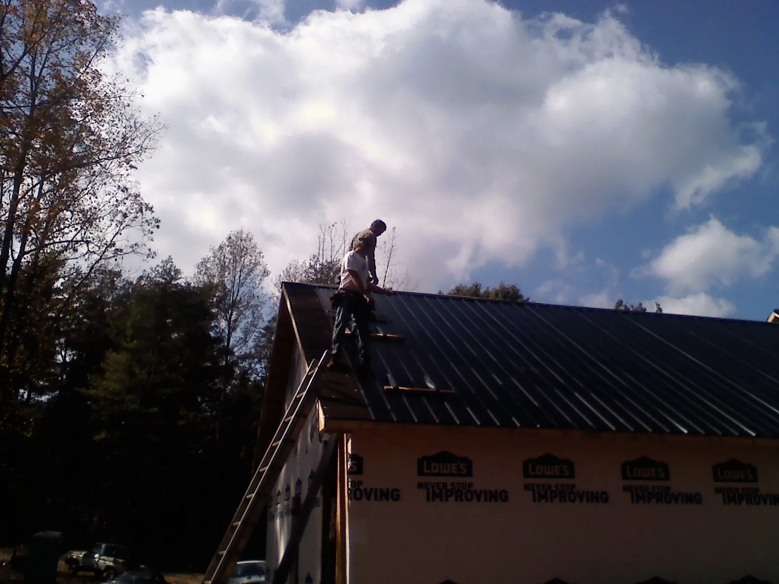 Roofer fastening dark metal panels high against a cloudy sky, from a Roof Inspection job in Waldorf