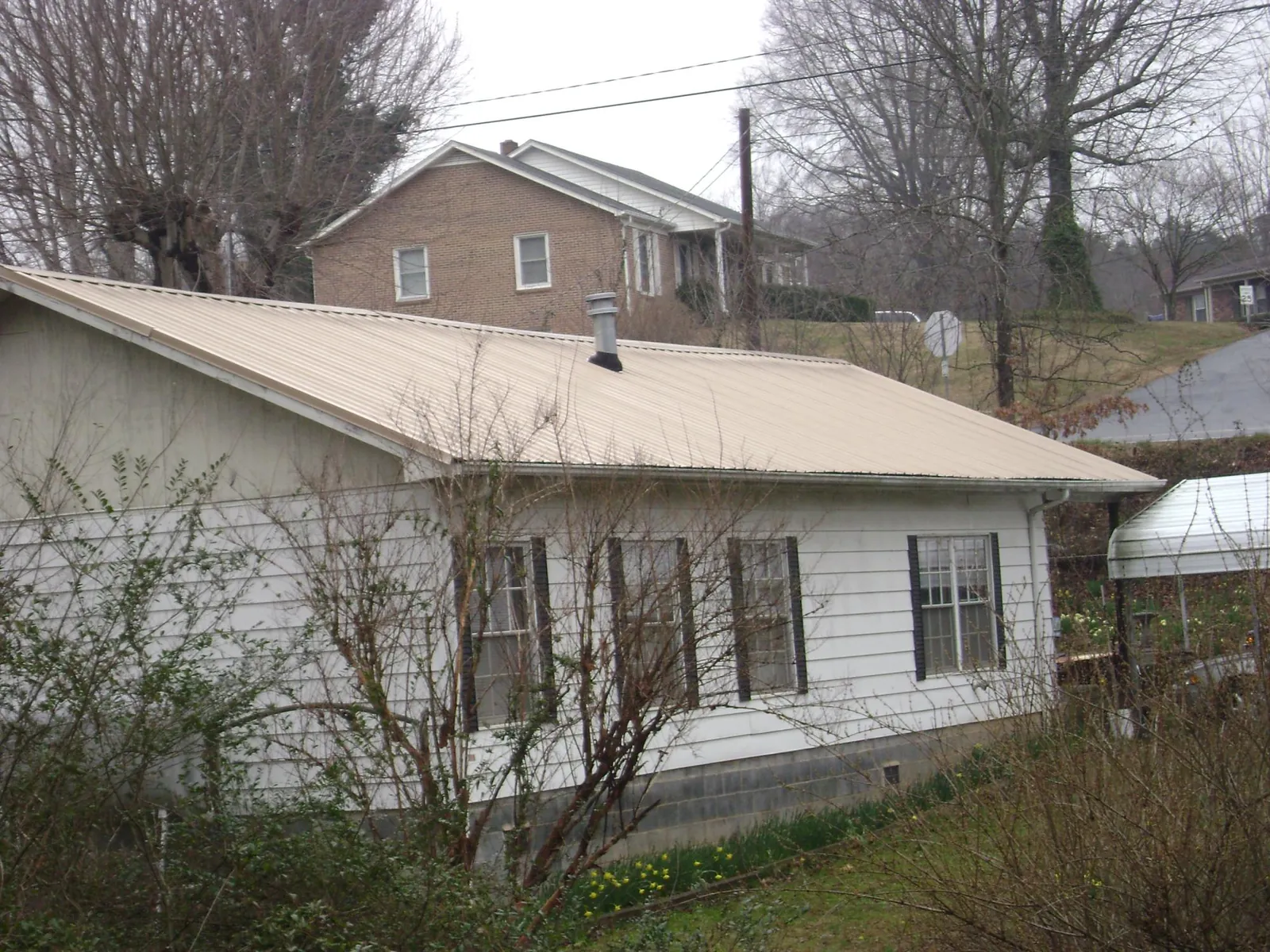 Tan metal roof on a white sided house set into a hillside — Commercial Roofing by Roofing Brothers in Waldorf